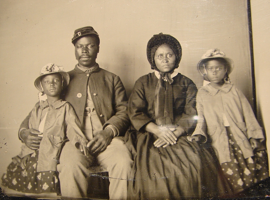 Black and white quarter-plate ambrotype photograph showing an African American Union soldier in uniform, wife in dress and hat, and two daughters wearing matching coats and hats. The soldier was originally unidentified but may be Sergeant Samuel Smith of the 119th United States Colored Infantry. In May 1863, U.S. Secretary of War Edwin Stanton issued General Order No. 143 creating the Bureau of U. S. Colored Troops. This image was found in Cecil County, Maryland, making it likely that this soldier belonged to one of the seven USCT regiments raised in Maryland. (Source: Matthew R. Gross and Elizabeth T. Lewin, 2010) This is the only known photograph of an African American Union soldier with his family.