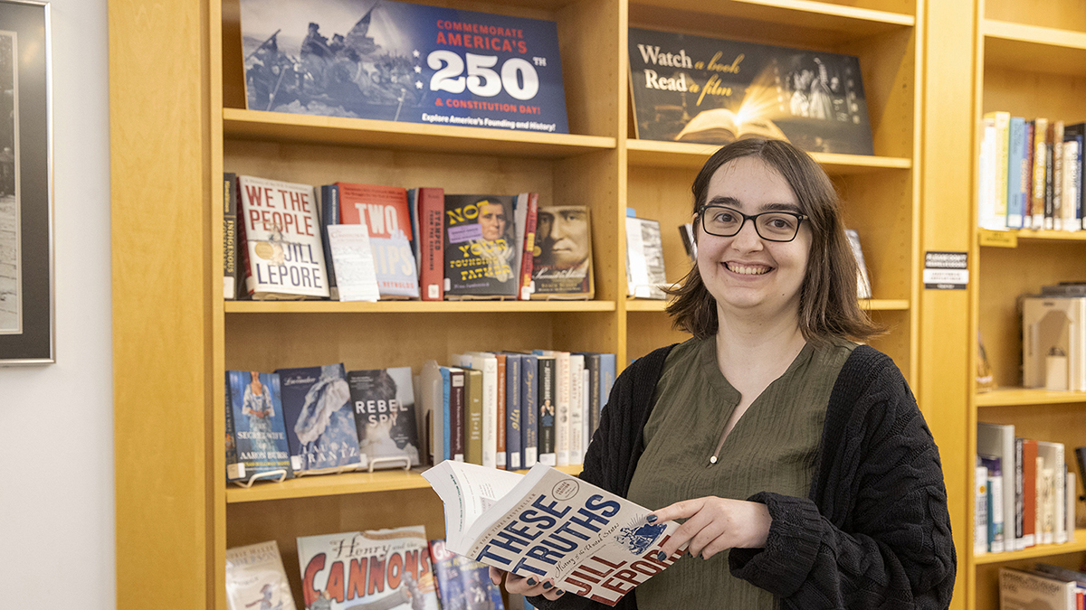 Librarian Moira Fiscus stands in Morris Library's browsing room holding a book about American history.