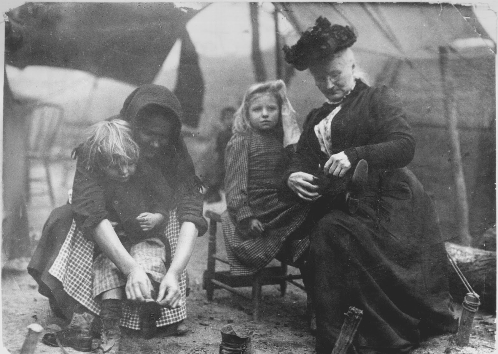 Mary Harris "Mother" Jones, a grandmotherly woman with her gray hair under a dark bonnet, ties the shoe of small girl seated in her lap.