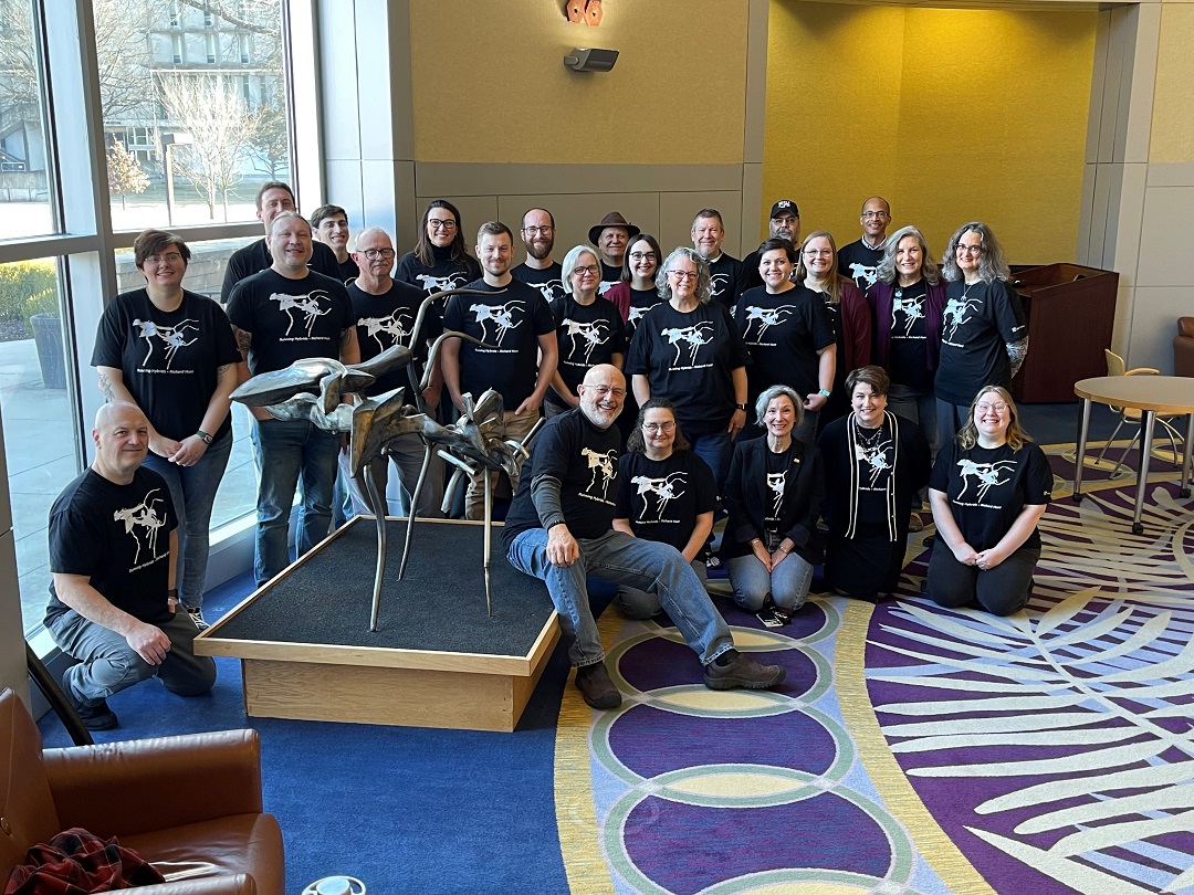 Group portrait of Morris Library staff members posed around Richard Hunt's Running Hybrids in the first floor rotunda, all wearing their matching Running Hybrids t-shirts.